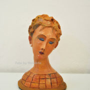 Scultura in terracotta di Anna Maria Acone con volto allungato, occhi chiusi e testa inclinata in stile Modigliani.