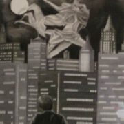 Dipinto monocromatico di Fiorenzo Isaia raffigurante un uomo affacciato di spalle verso uno skyline notturno con una figura femminile eterea che vola nel cielo vicino alla luna.