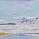 Spiaggia con bandiere al vento, mare mosso e pontile sullo sfondo.