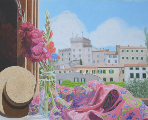Davanzale con cappello, vaso di fiori e tessuto colorato, vista su case e torre di Rosignano sotto cielo azzurro.