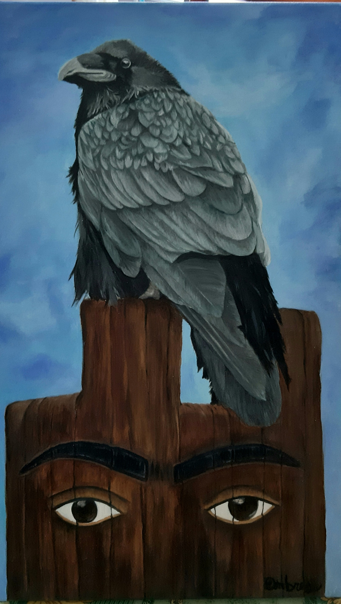 Primo piano di un corvo grigio e nero posato su un totem di legno scuro con due grandi occhi umani intagliati, dipinto da Ombretta Montanelli, sfondo con cielo azzurro sfumato.