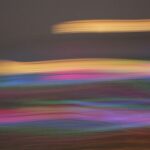 Composizione astratta con scie luminose orizzontali dai toni rosa, viola, blu, verdi e dorati su fondo scuro, caratterizzata da forte effetto di movimento e sfocatura.