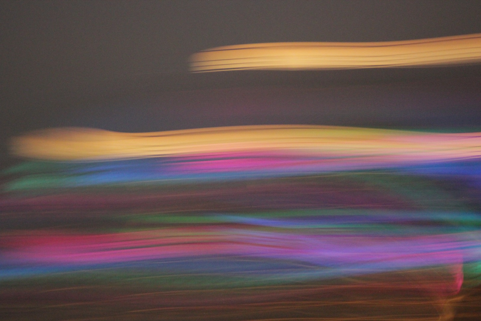 Composizione astratta con scie luminose orizzontali dai toni rosa, viola, blu, verdi e dorati su fondo scuro, caratterizzata da forte effetto di movimento e sfocatura.