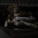 Fotografia di Rebecca Levi raffigurante mozziconi di sigaretta e piccoli rifiuti raccolti in un posacenere urbano ripreso in luce notturna.